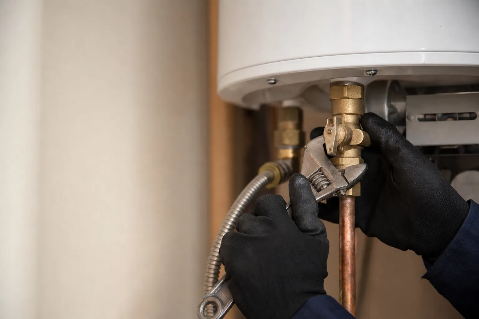 Gloved hands servicing the gas control valve on a water heater